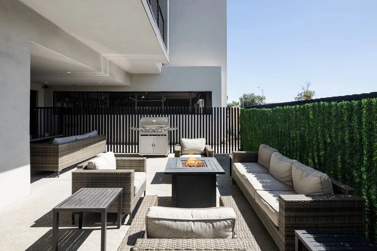 A welcoming exterior communal space with a modern fire pit, grill, and ample comfortable outdoor seating. The area is designed for barbecues, evening gatherings, and cozy conversations under the stars.