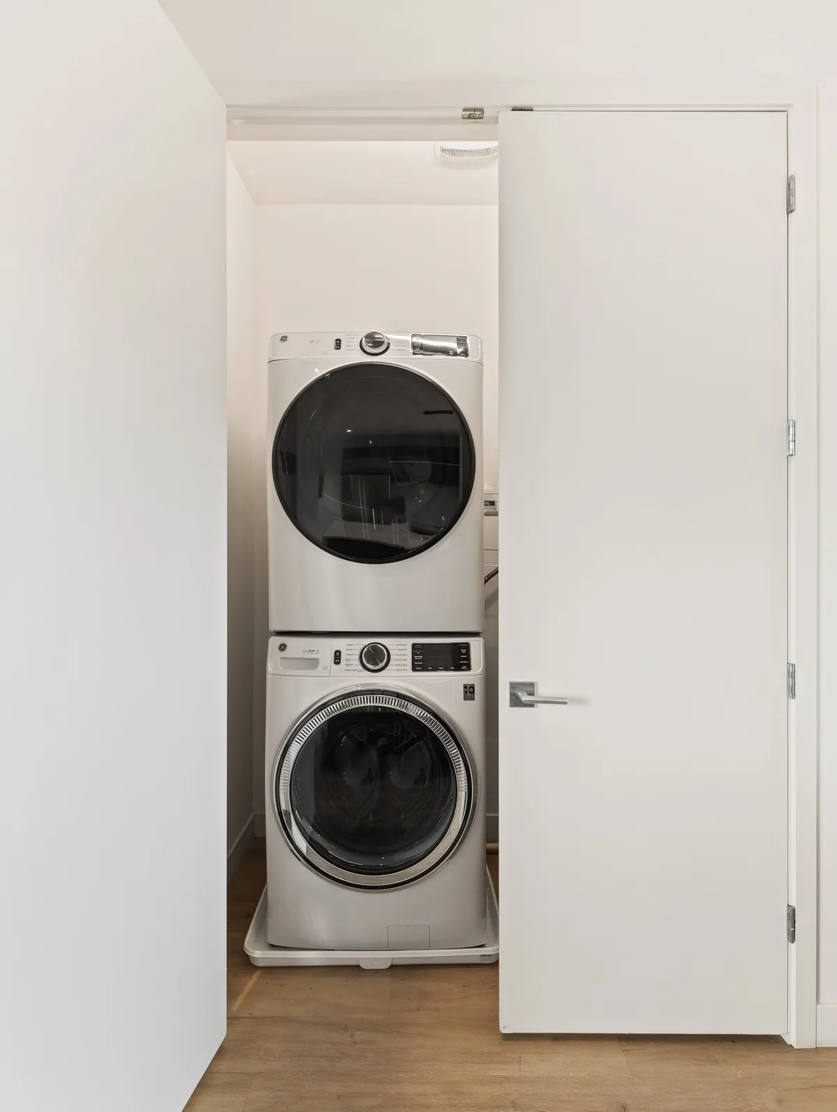 A bright, efficient laundry nook with a stacked washer and dryer, white doors, and a light wooden floor—exuding a sense of organization and ease.