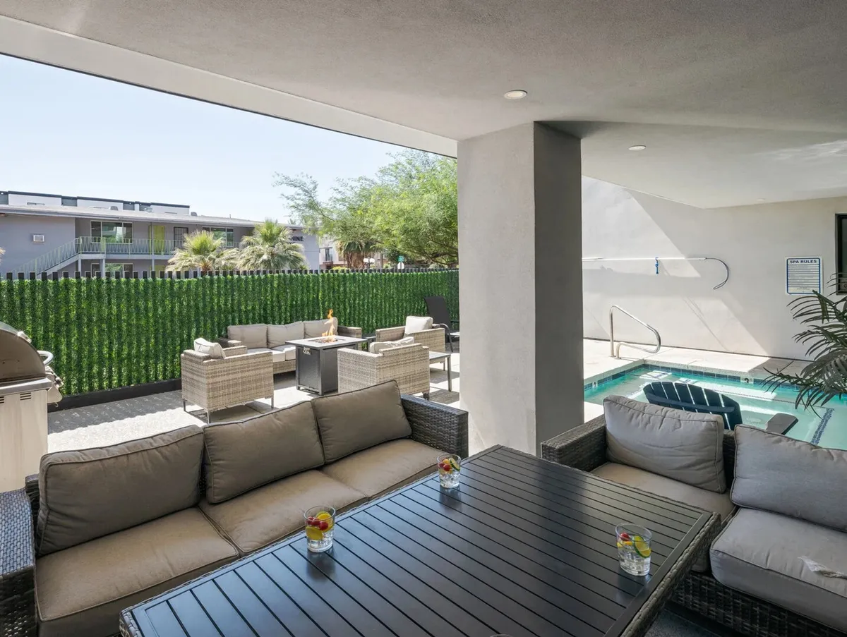 A stylish outdoor community space featuring comfortable seating, a swimming pool, lush greenery, and a table with drinks. The area is ideal for relaxing, socializing, and barbecuing, especially in the evening light.