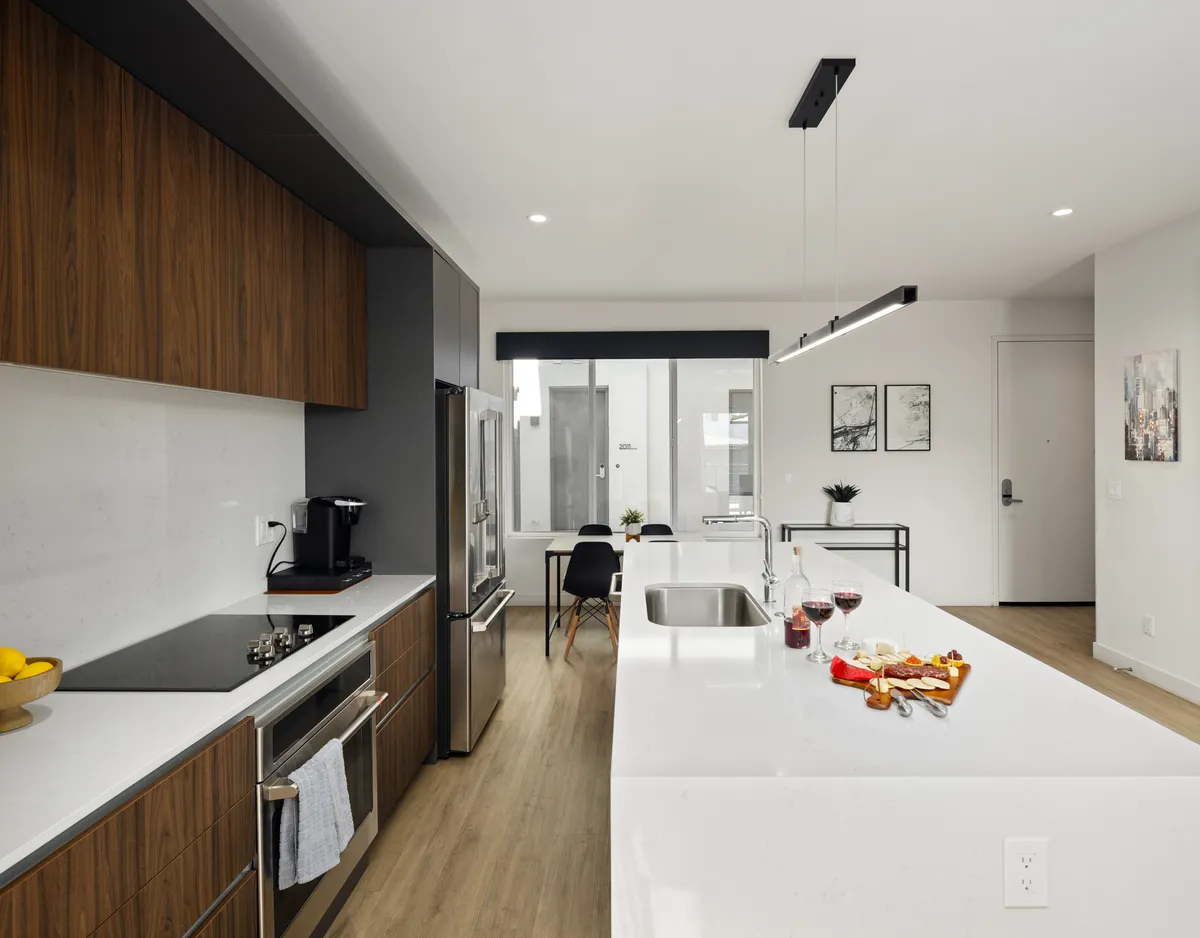 A bright and inviting interior scene showcasing a spacious kitchen with a large island, modern stainless steel appliances, and adjacent dining area. Decorative art adorns the walls, and the space is arranged for easy interaction between the kitchen, dining, and living zones.