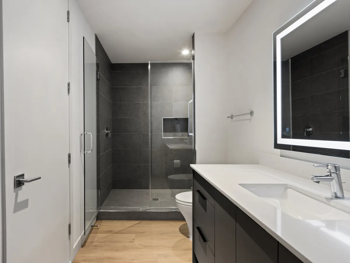 A contemporary ensuite bathroom with a sleek glass stand-in shower, modern vanity with a backlit mirror, and natural sunlight streaming in. The space feels spa-inspired and calming, ideal for self-care routines after a long day.
