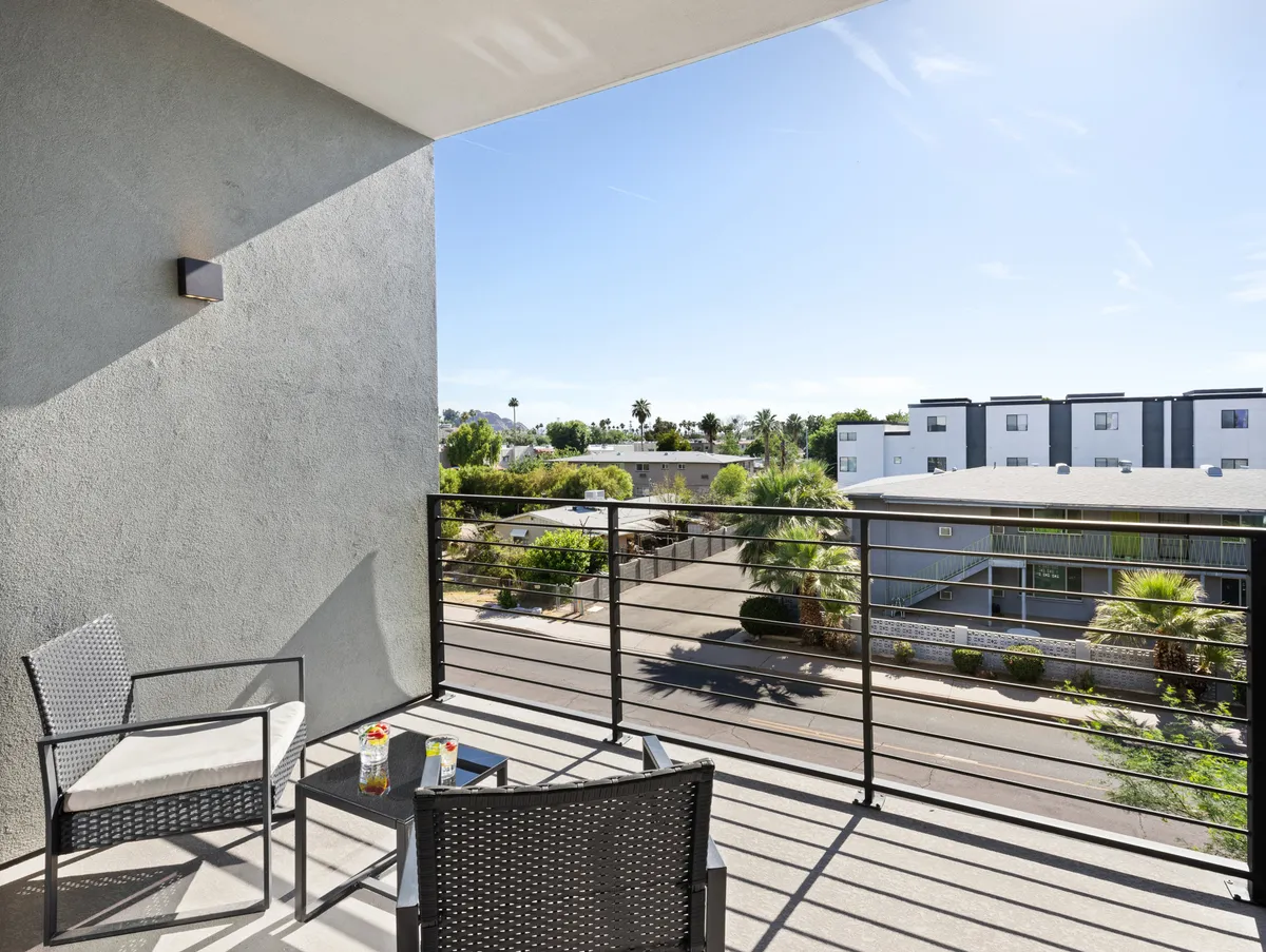 A serene private balcony scene with comfortable seating, a table with drinks, and a view of palm trees and nearby buildings. The setting is perfect for sipping coffee in the morning, unwinding at sunset, or enjoying conversation with friends.