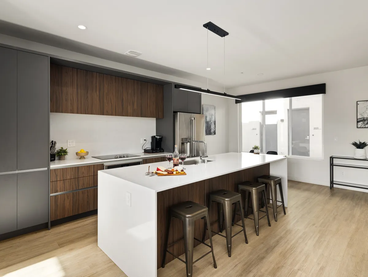 A contemporary kitchen space with an island countertop, bar stools, modern kitchen appliances, and a window offering a pleasant view. The area is well-lit and designed for both functionality and social gatherings.